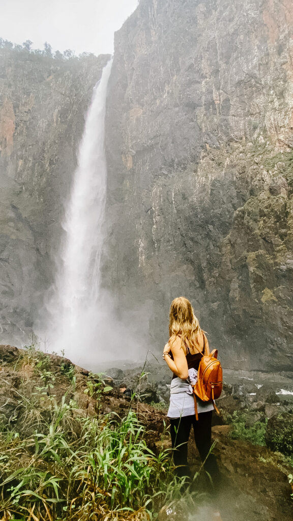 życie w australii, dziewczyna z plecakiem stoi przy wodospadzie wallaman 